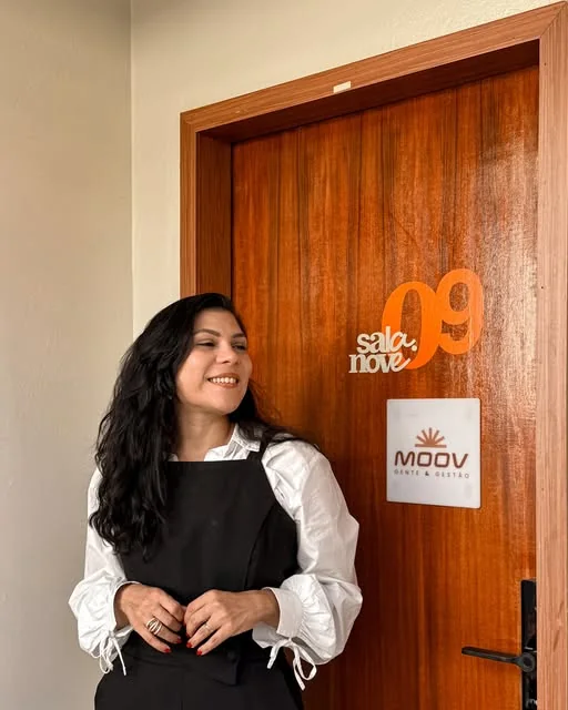 Profissional da MOOV sorrindo ao lado da porta da sala com o logotipo da empresa